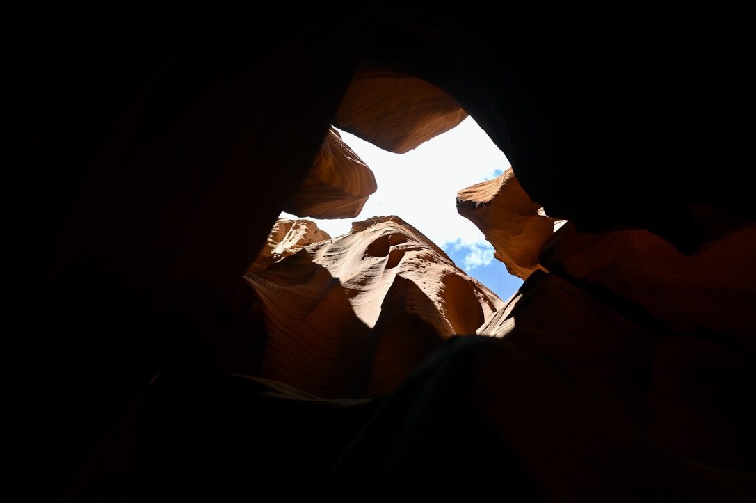 An X shaped opening looking at the sky above, from beneath soaring red canyon walls.