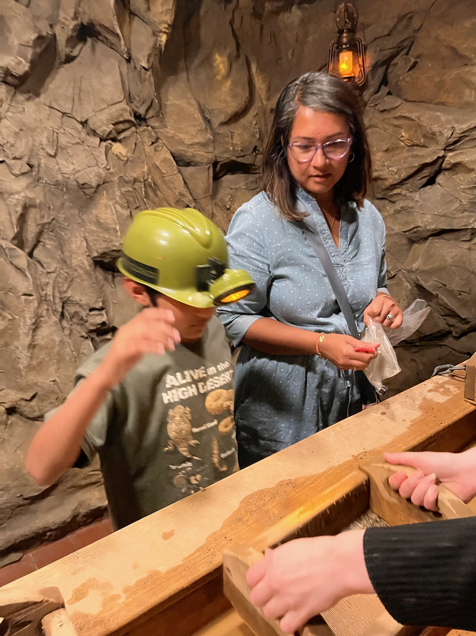 Woman and boy inside a rocky cave structure looking at a station that is mining for precious rocks from flowing water.