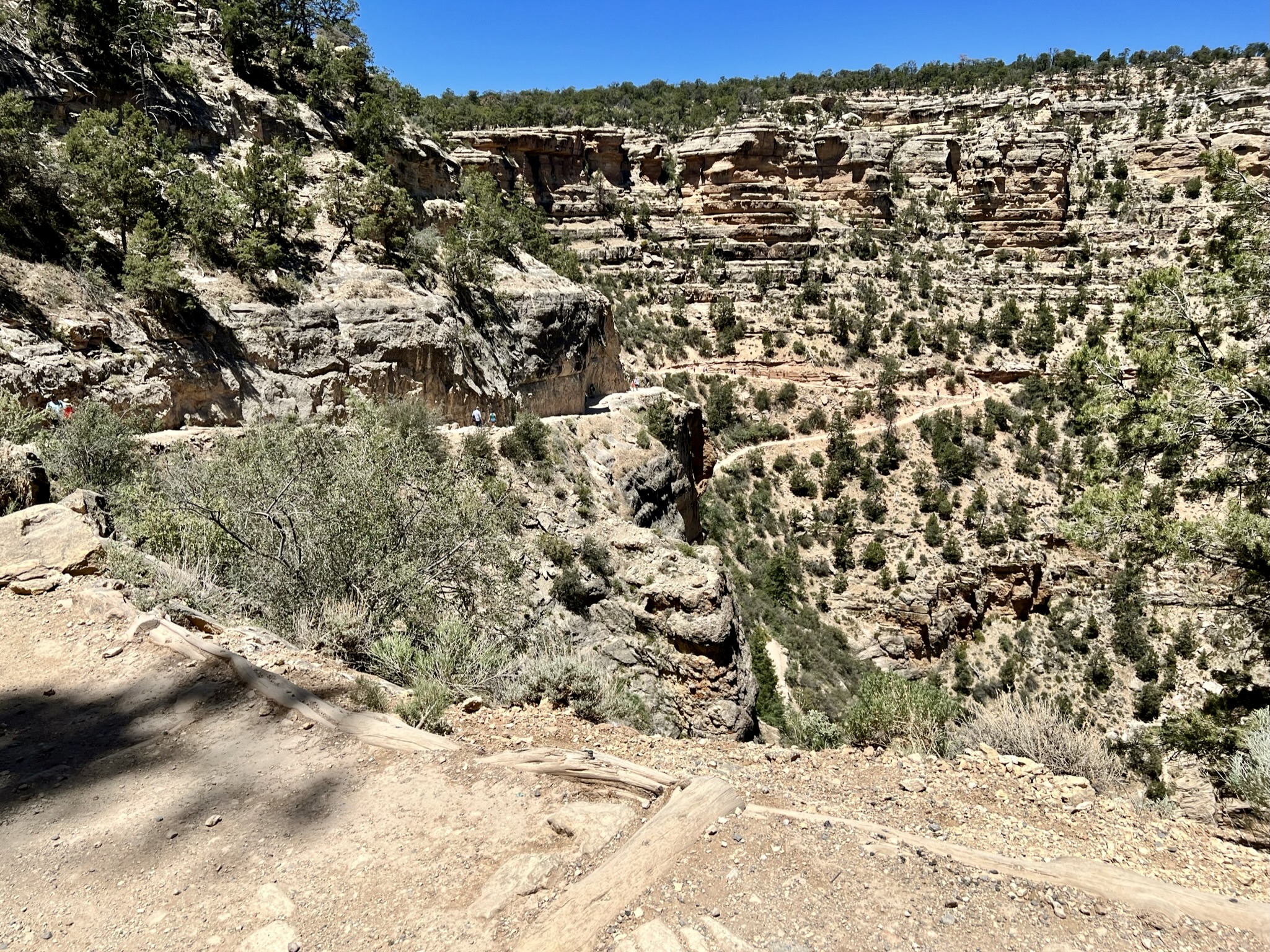 View down a trail of desert canyon walls of sedimentary rocks covered with shrubs.