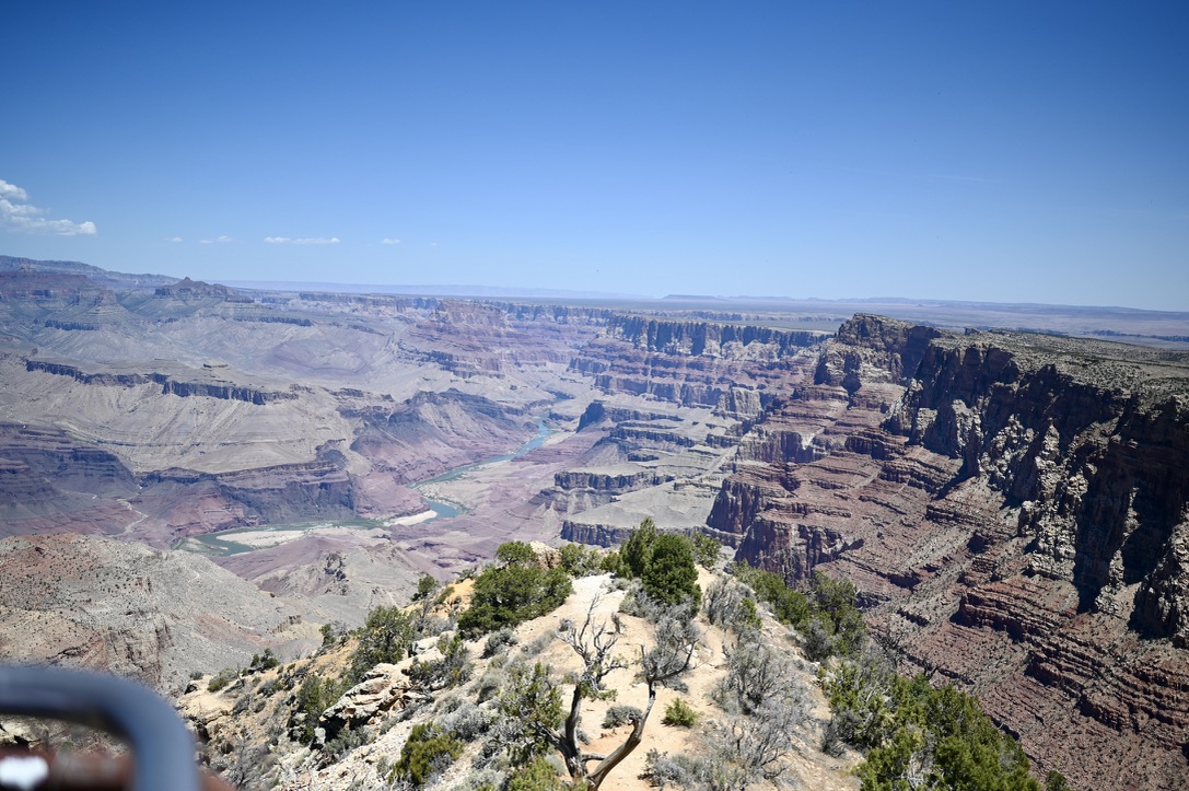 Desert view viewpoint of The Grand Canyon with big hill of light sand and short shrubby trees.