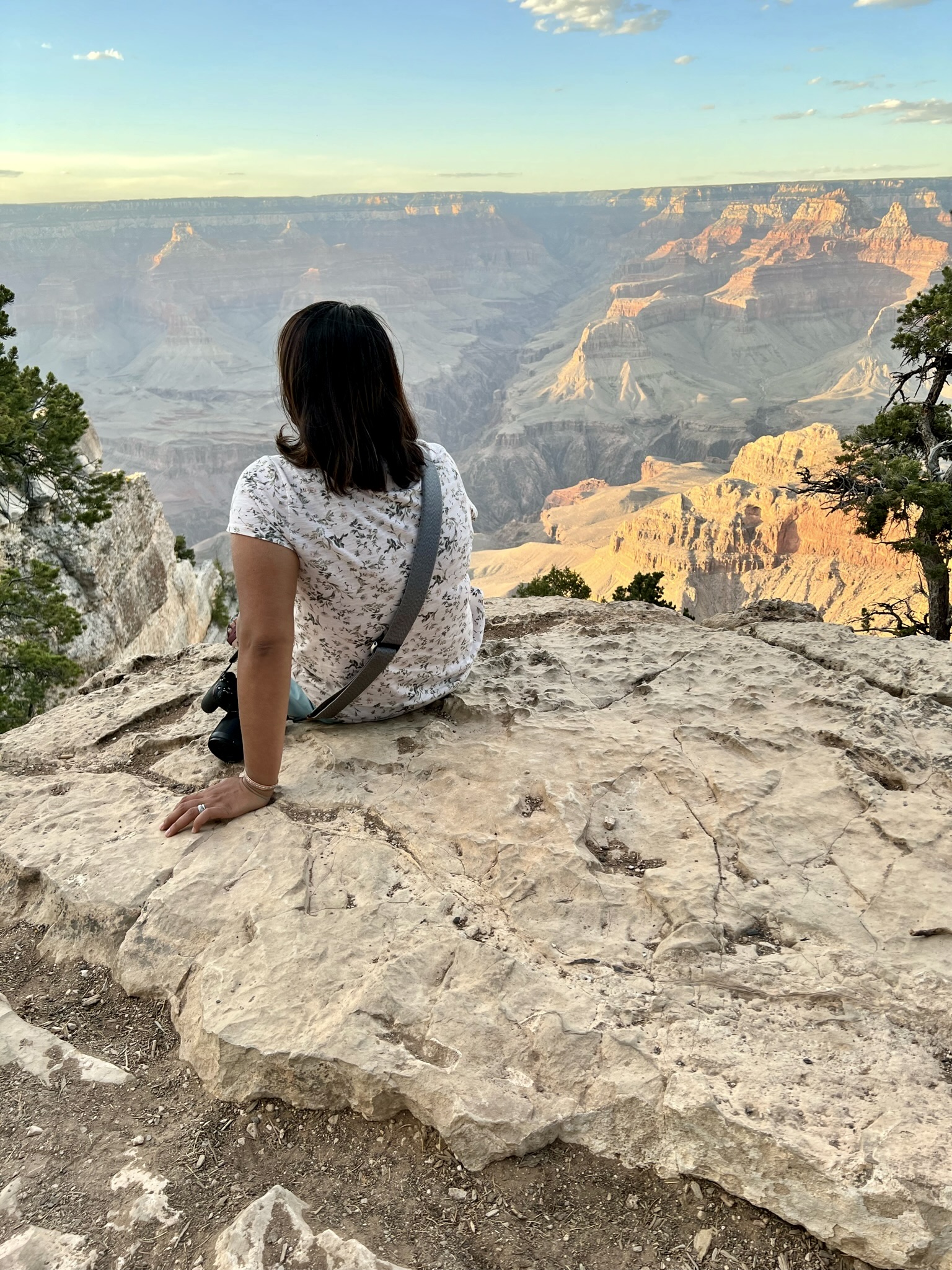 Grand canyon view with red, orange and gray canyon walls and woman sitting in foreground with her back to the camera on sandstone slab