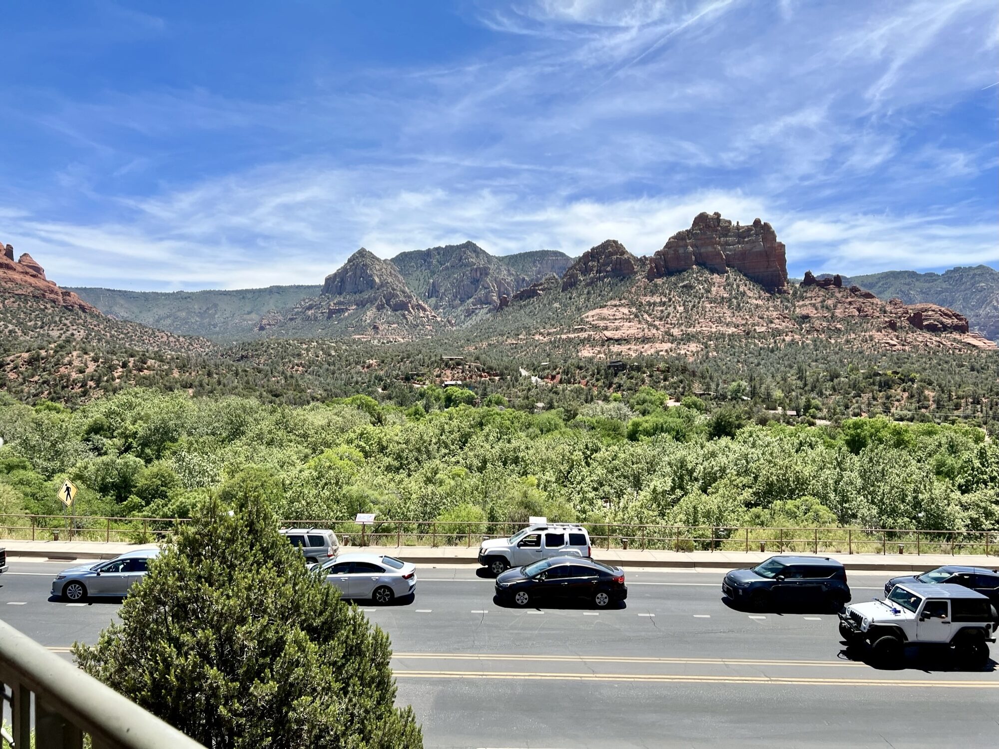 Red rock buttes rising above green desert, seen over a road in Sedona