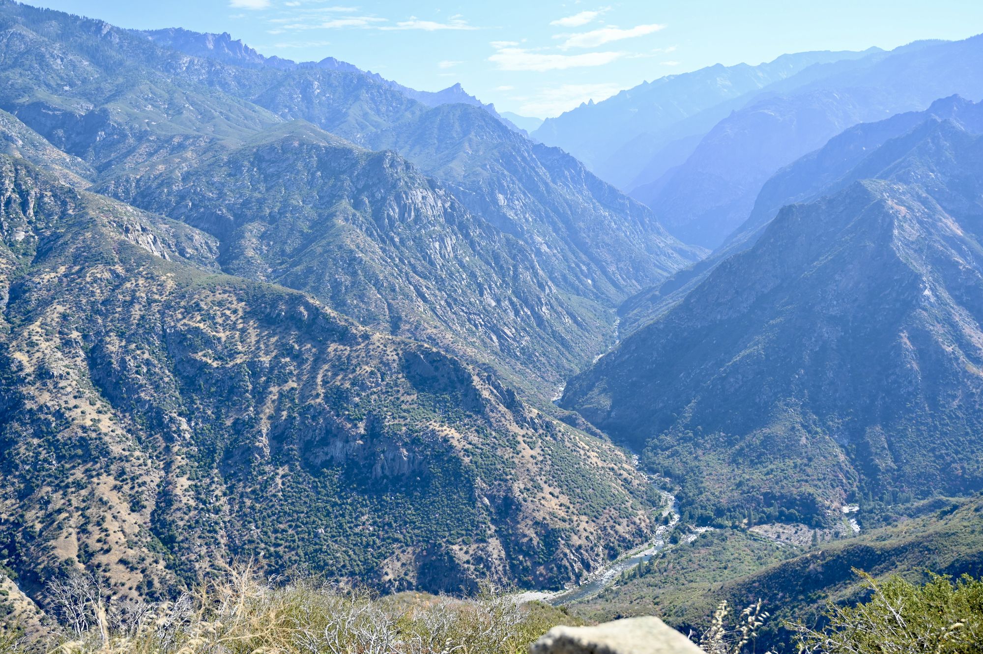 A deep V-shaped canyon with a river at the bottom and layered mountain ridges fading into the distance.