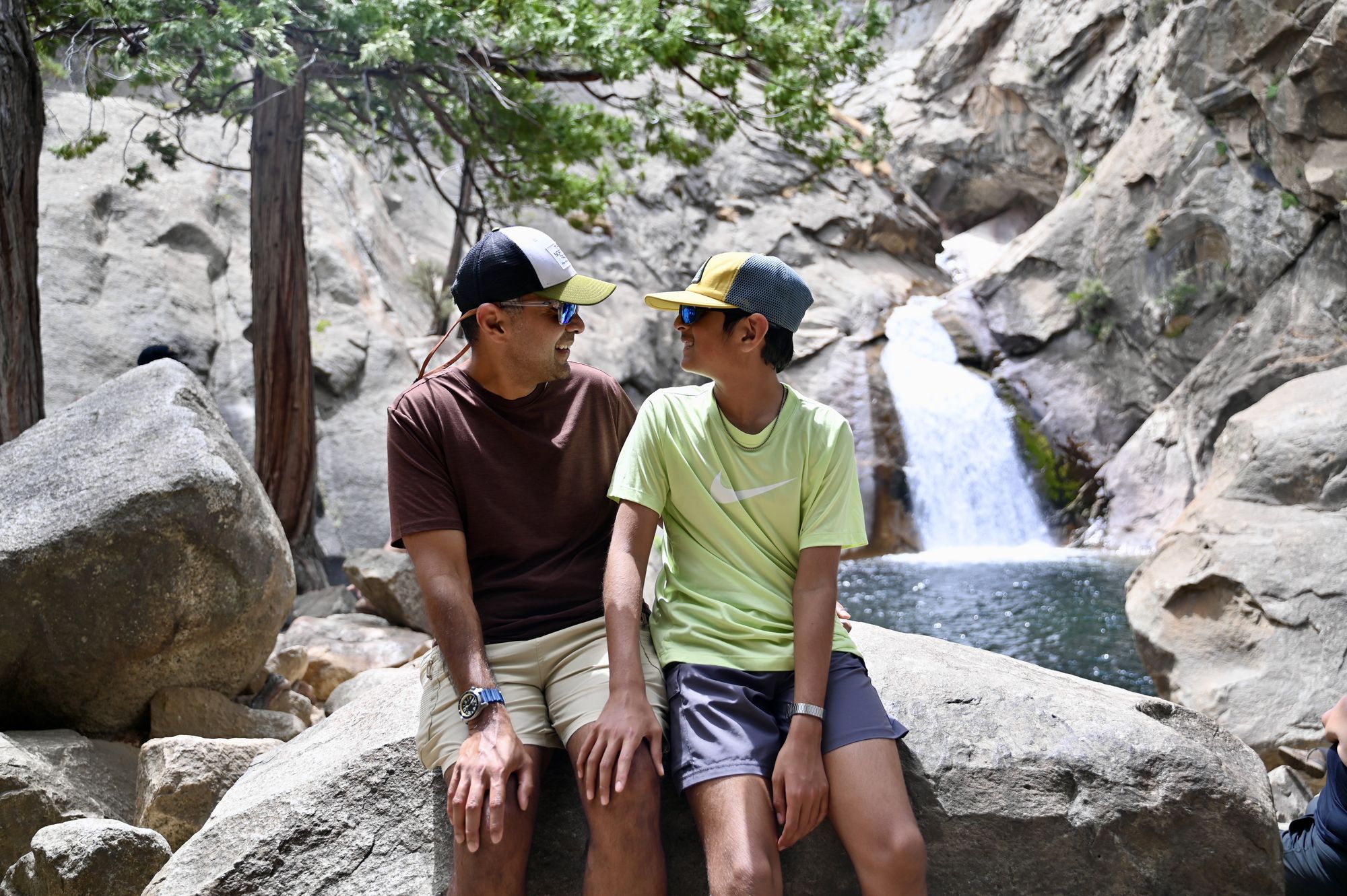 Our son and his dad sitting on a boulder, smiling at each other, in front of Roaring River falls pouring into a pool.