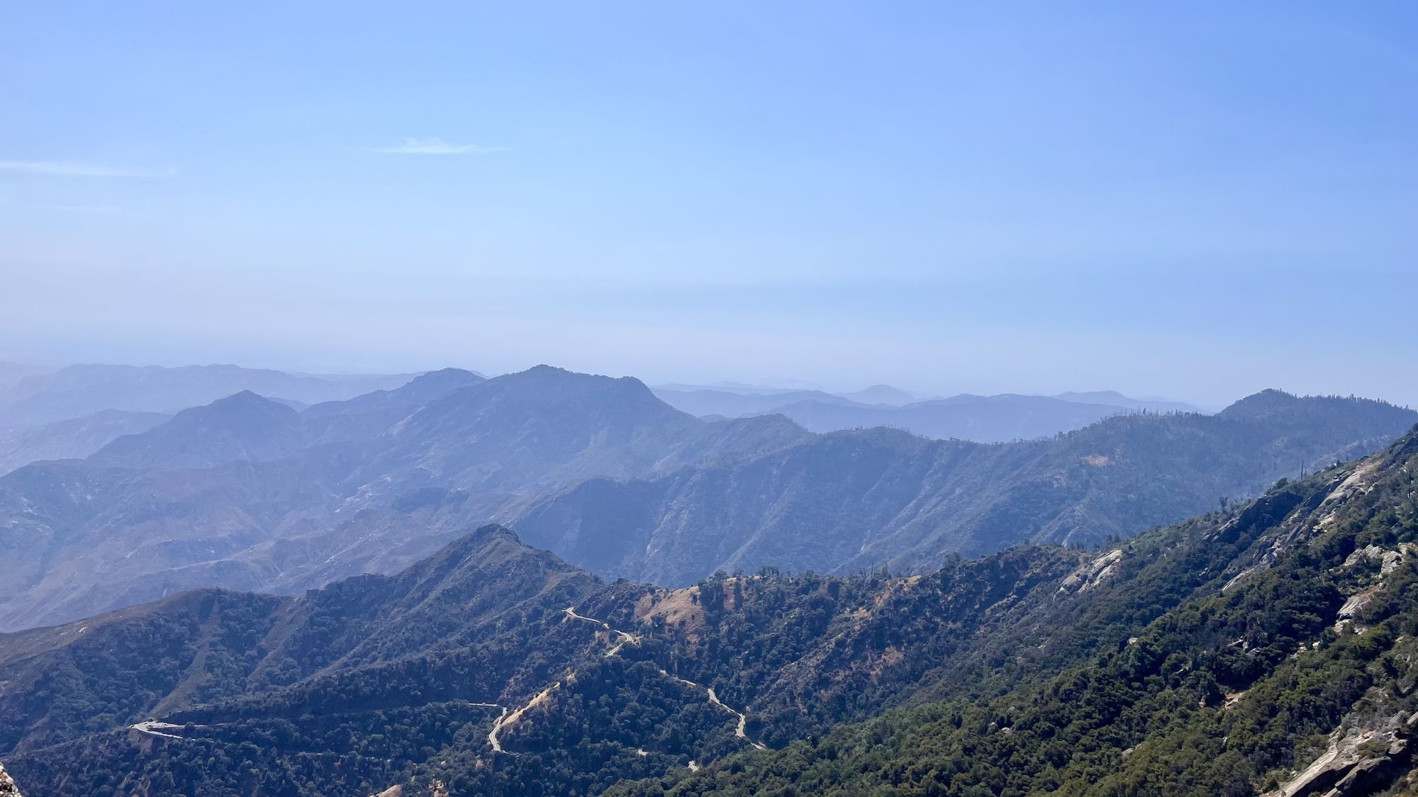 Layers of hazy blue mountain ridges seen from partway up the Moro Rock trail, with a switchback road below.
