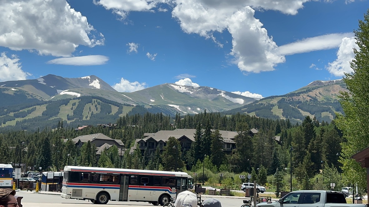 Breckenridge mountains in background with buildings in the tree line and bus passing in the middle with other vehicles around