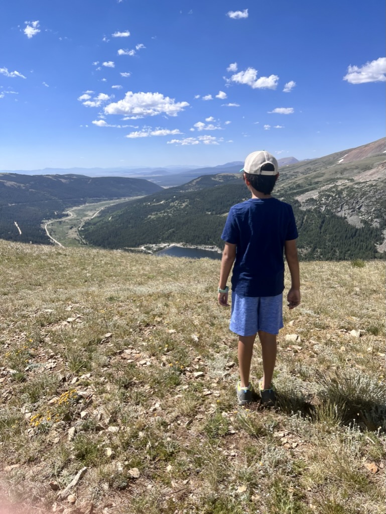 Boy standing on the meadow overlooking mountains and valley in Hoosier pass trail hike