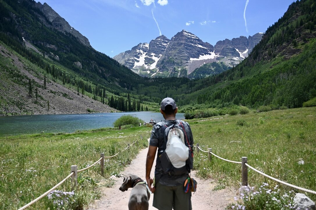 Man and dog on a trail toward Maroon Lake, with the snow-streaked Maroon Bells peaks ahead