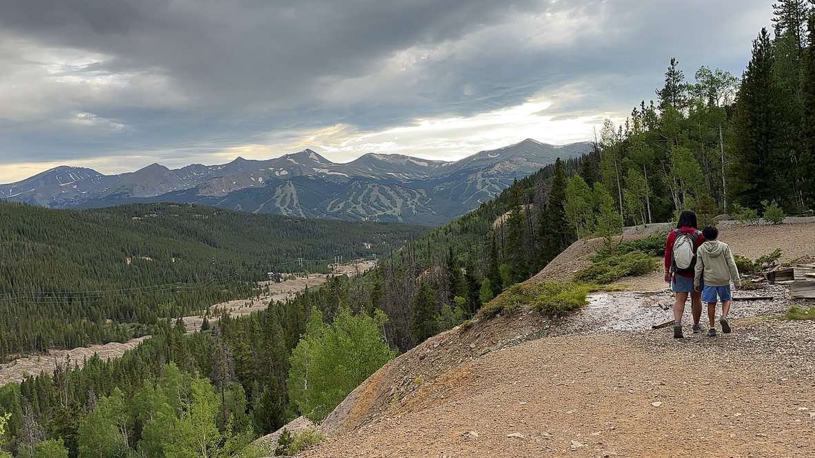 Woman and boy walking along the trail ridge overlooking a valley with mountains in the background