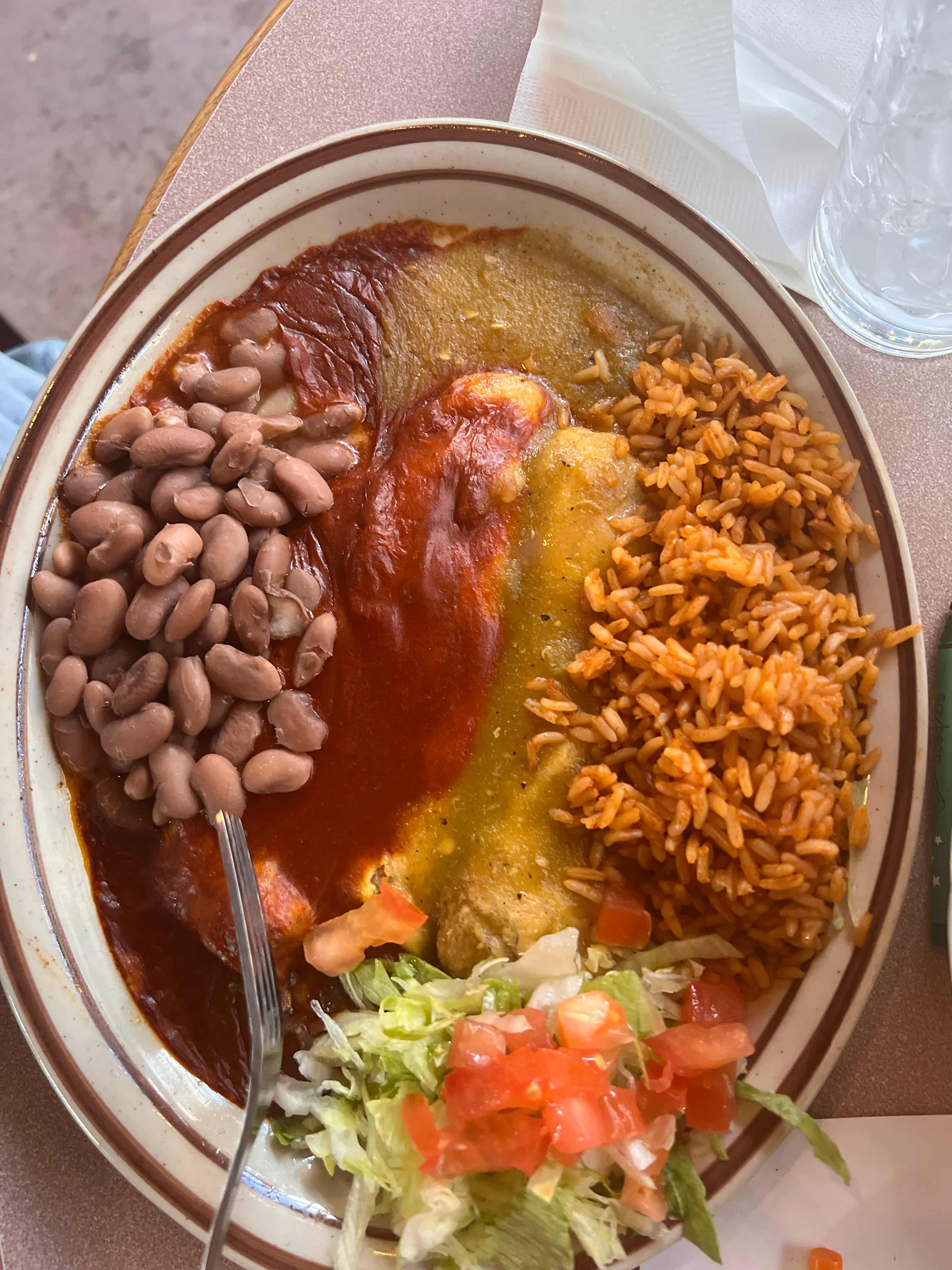 Plate with food containing rice, beans, pico, salad, and green and red sauces