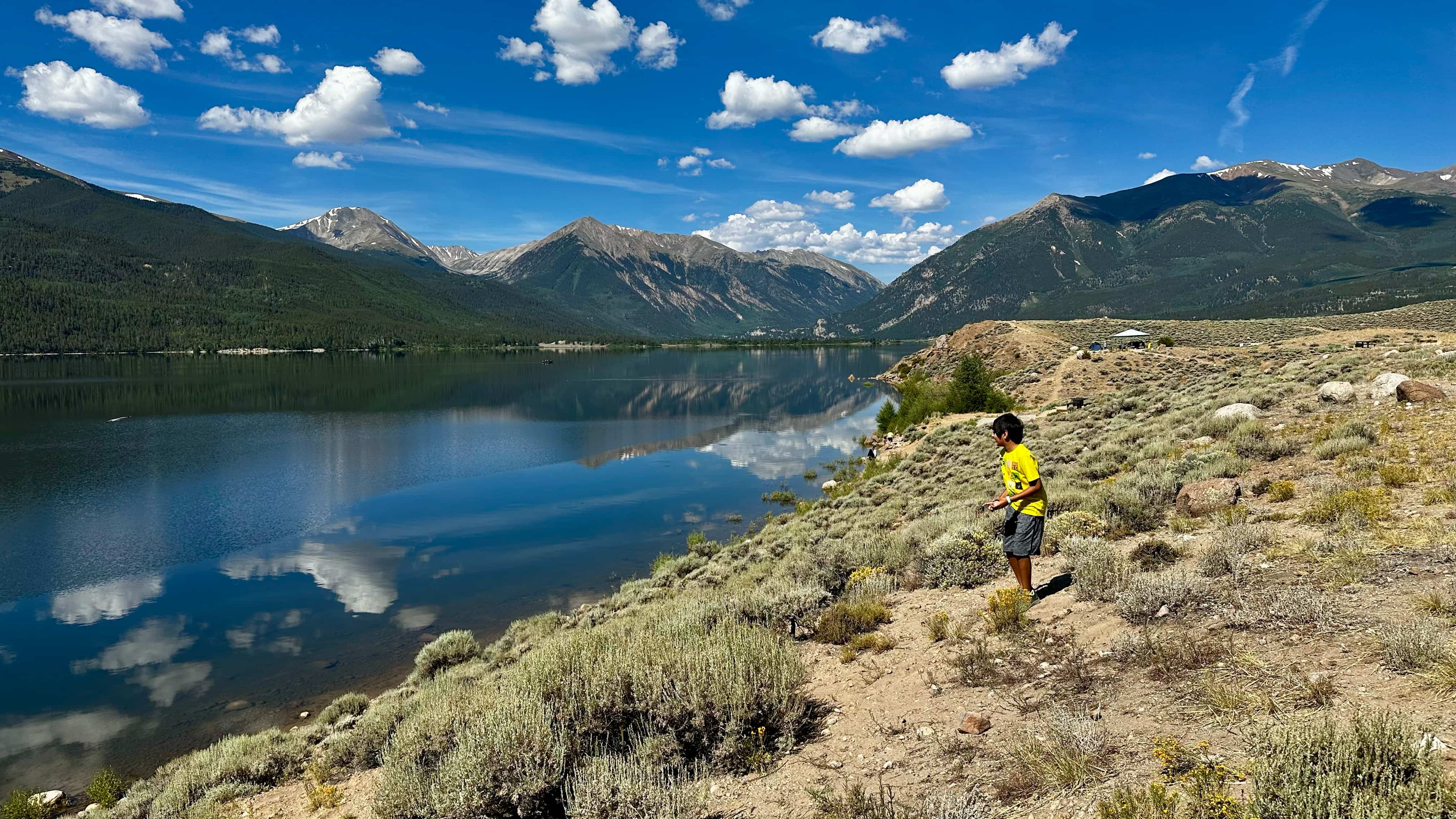 Boy standing on the banks of a lake with mountains in the background