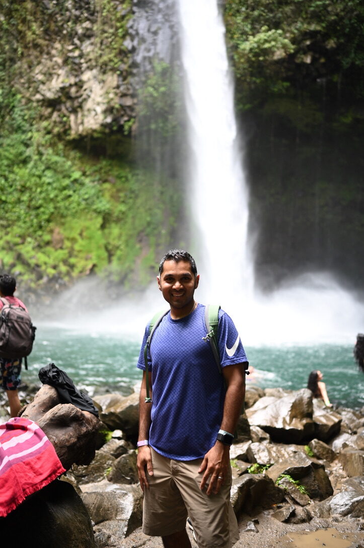 Man standing on the rocks at the base of the powerful waterfall