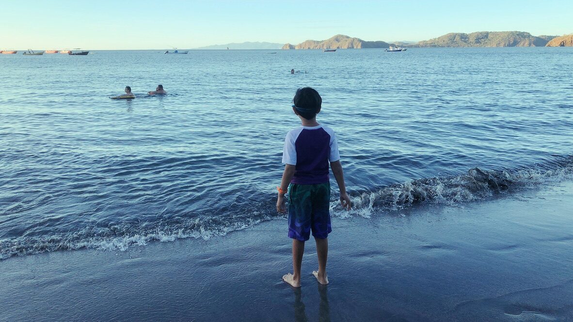 Boy standing at the water’s edge on Playa Hermosa in the evening