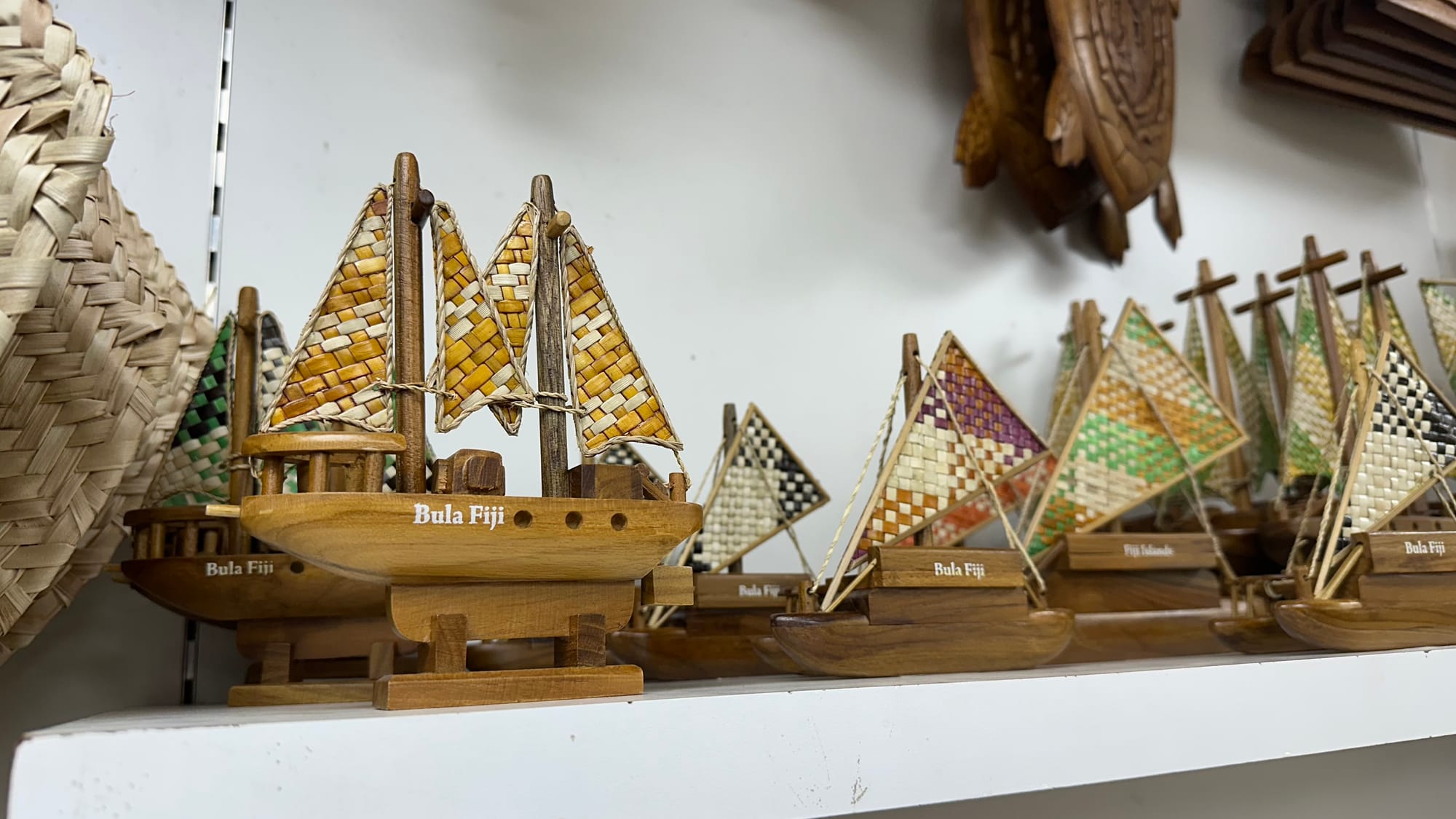 A shelf of carved wooden model sailing boats with woven palm-leaf sails, each labelled “Bula Fiji”.