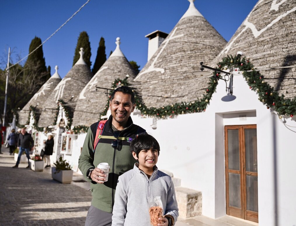 Man and boy smiling on a street of white trulli with conical stone roofs