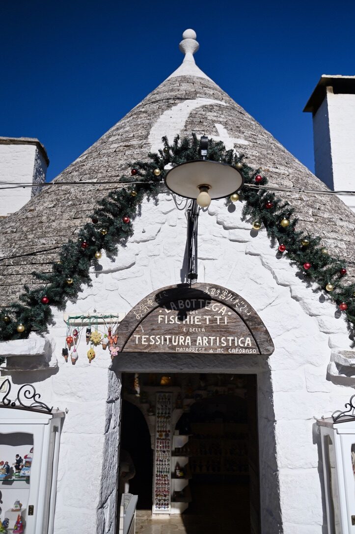 A whitewashed trullo with a conical stone roof, decorated with garlands