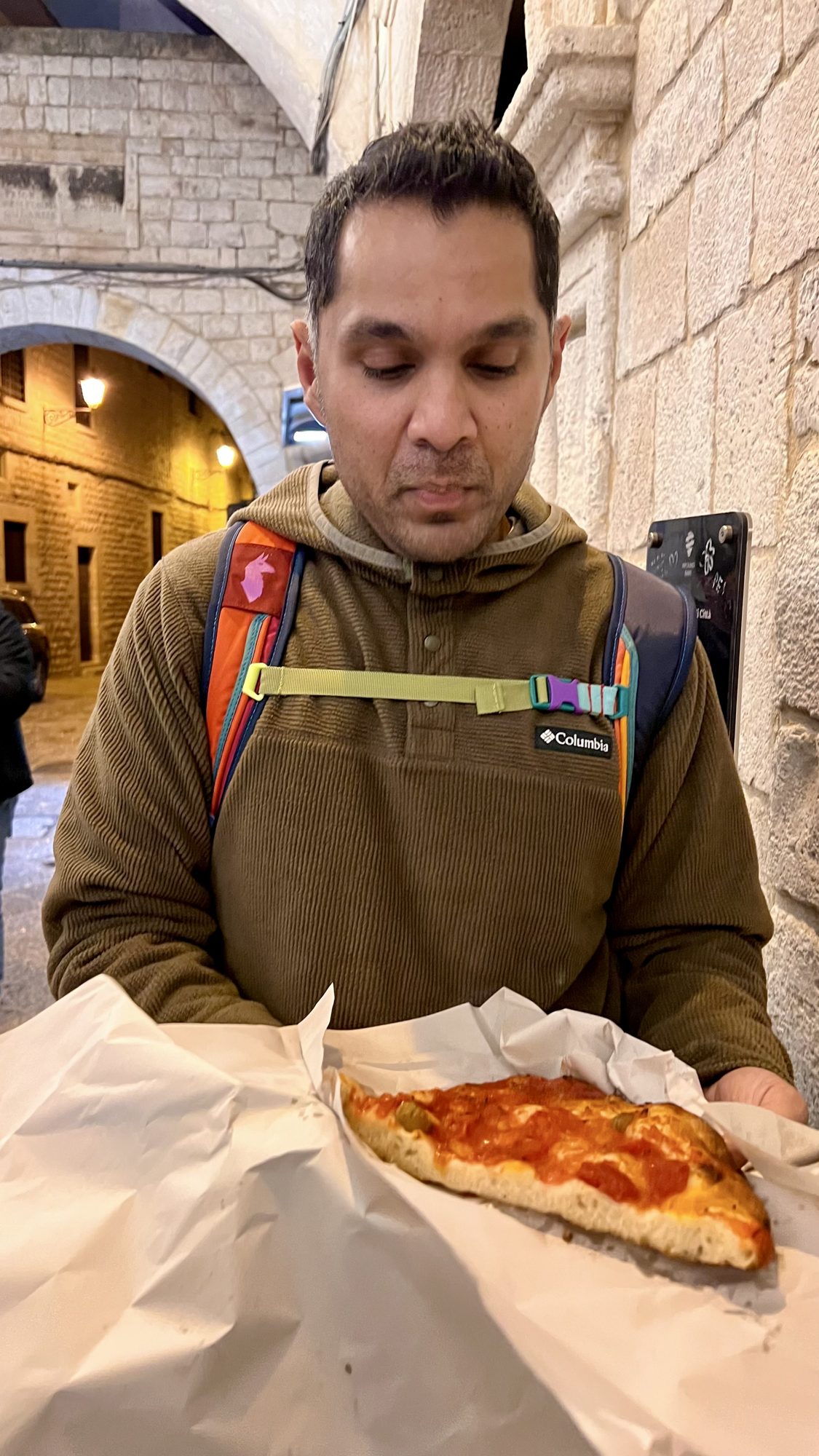 Man holding a slice of tomato focaccia wrapped in paper