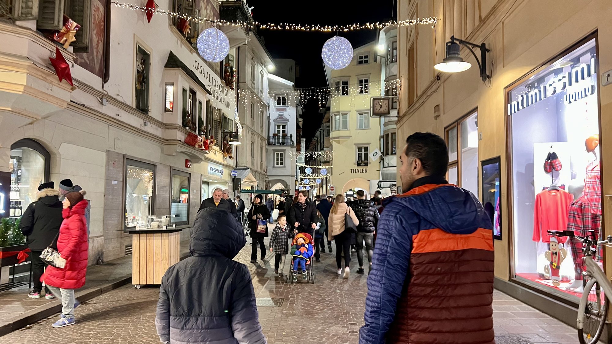 Shoppers on a lit-up street in Bolzano’s old town at night