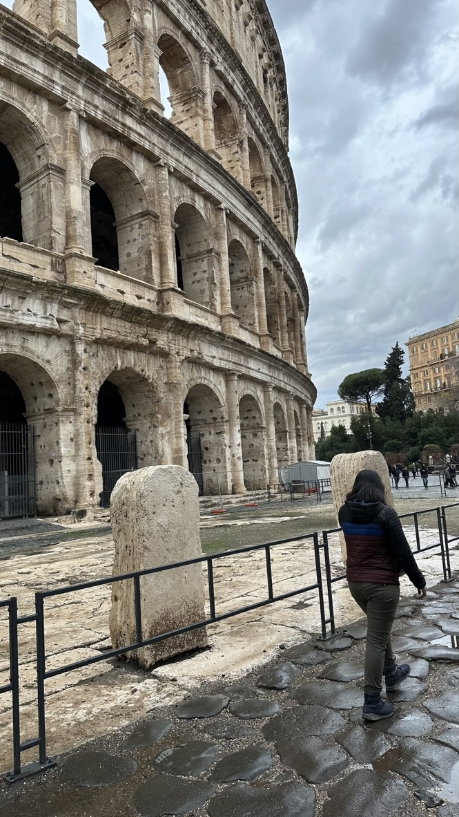 Lady walking on cobble stone pathway on the side of a perimeter in front of the Roman world wonder, the Colosseum