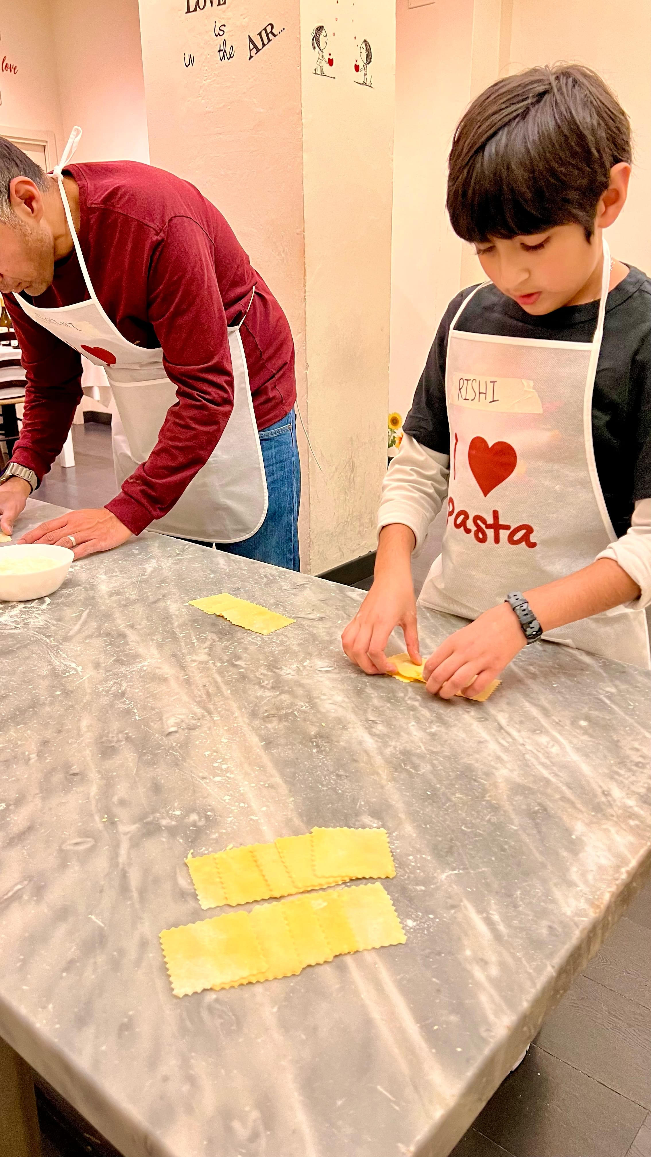 Boy and man standing in front of a marble food prep table making pasta shells