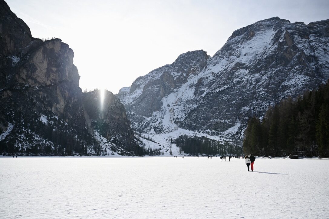 People walking across the frozen, snowy lake between steep mountains