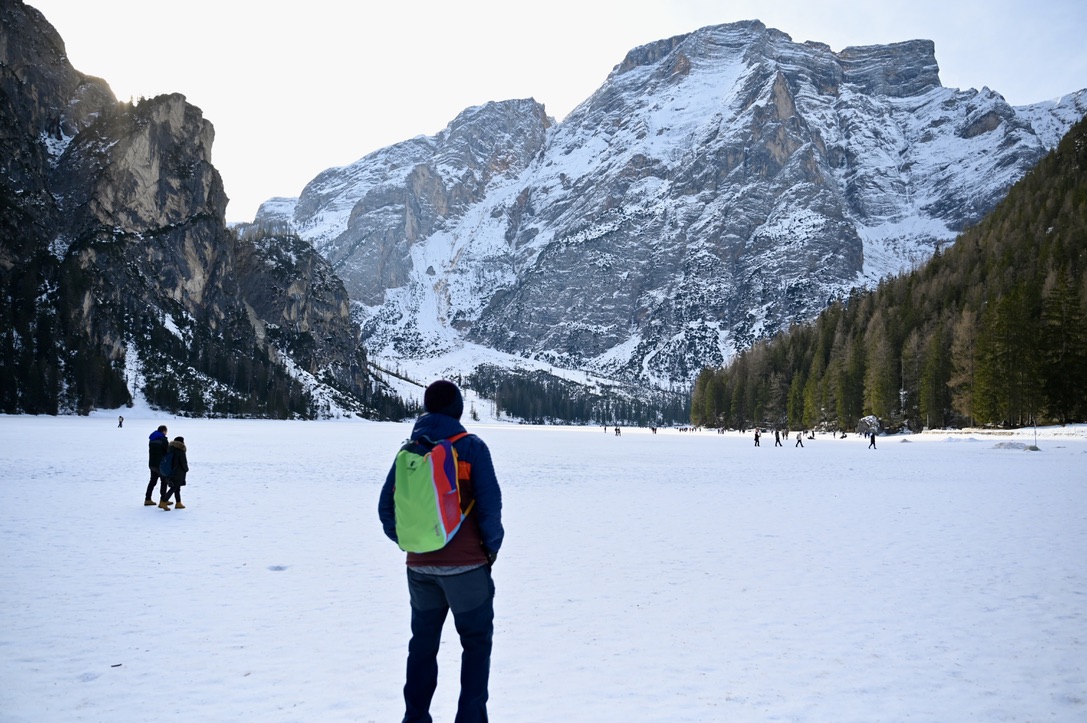 Man standing on a frozen lake with backpack looking at the snow covered mountains in the distance