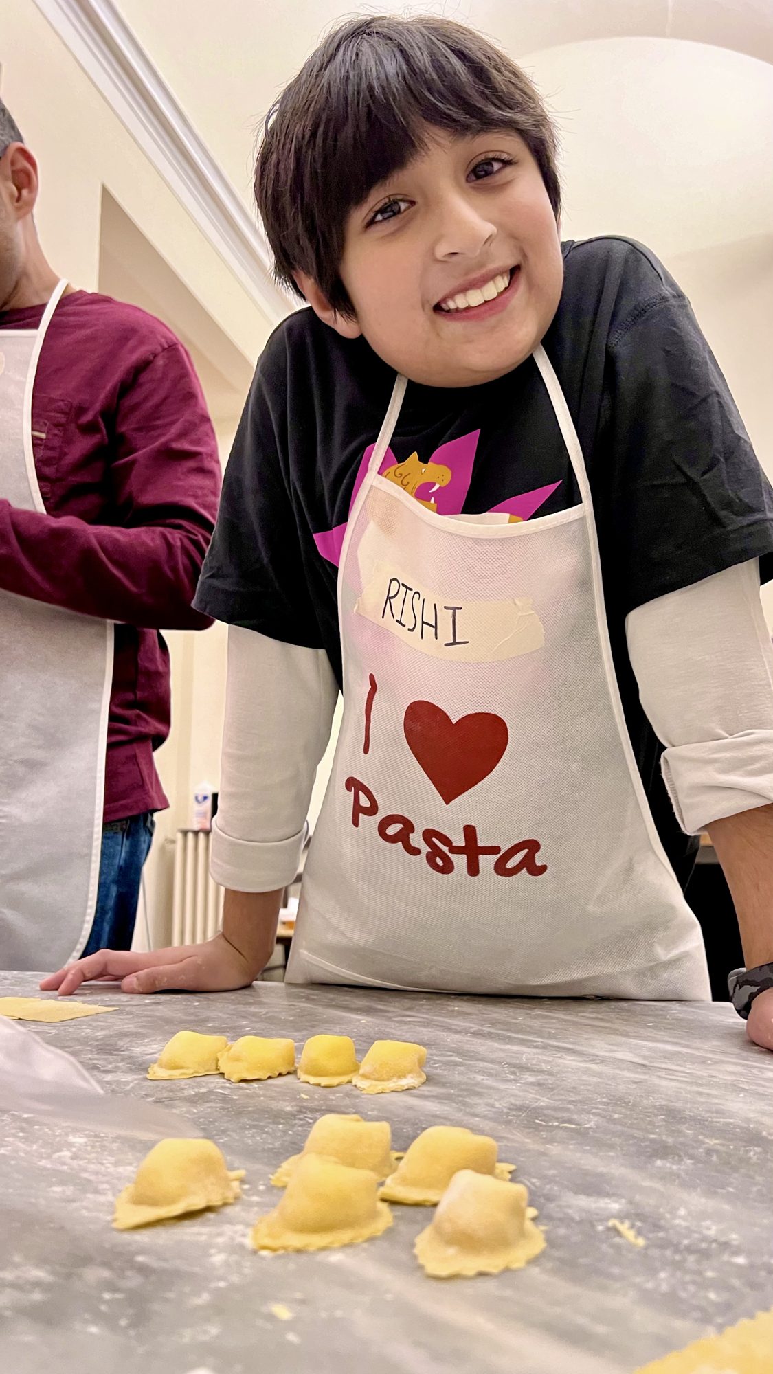Boy in an apron smiling over a tray of handmade ravioli