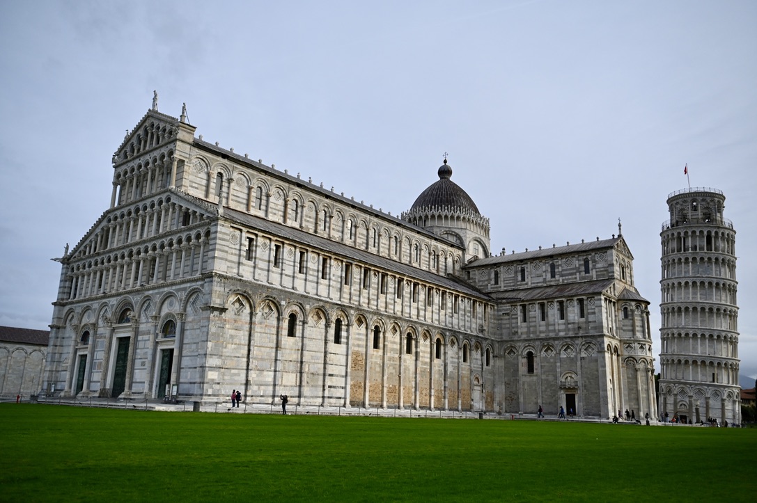 White marble cathedral with leaning tower of Pisa in the background and green lawn in the foreground