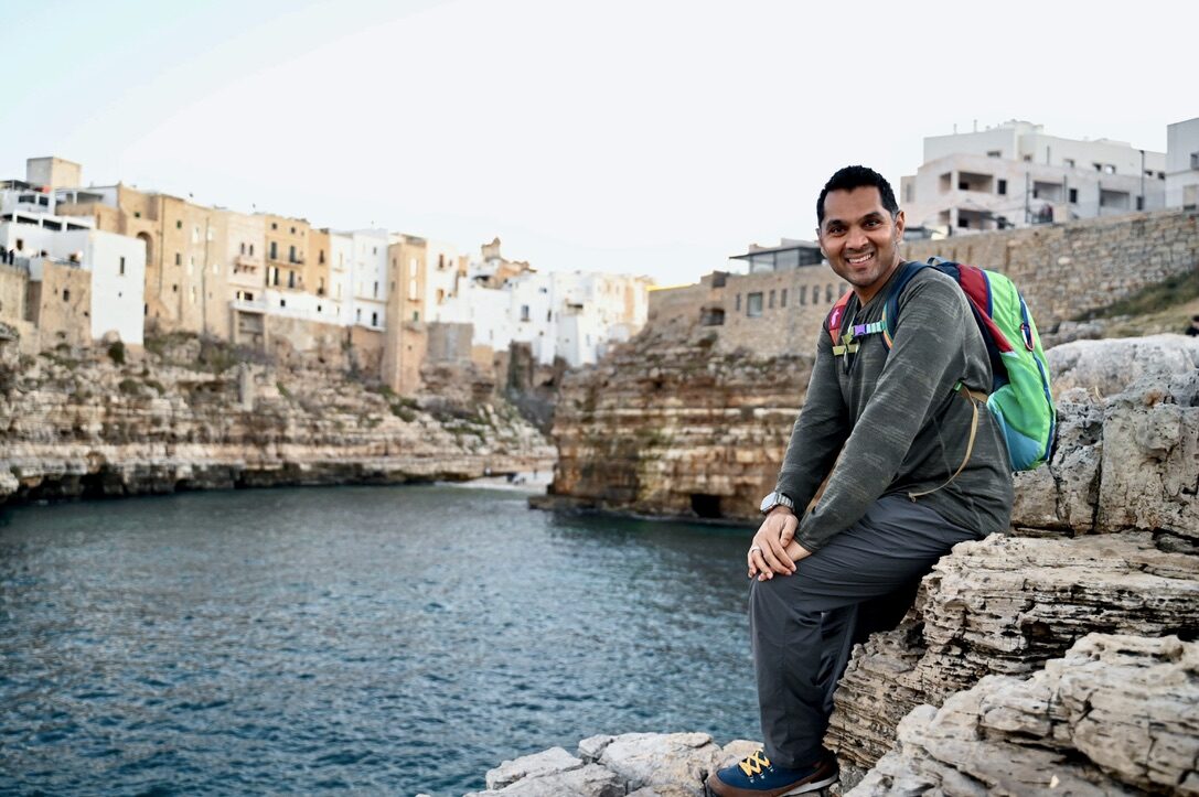 Man sitting on the rocks with the town and its cliffs behind him