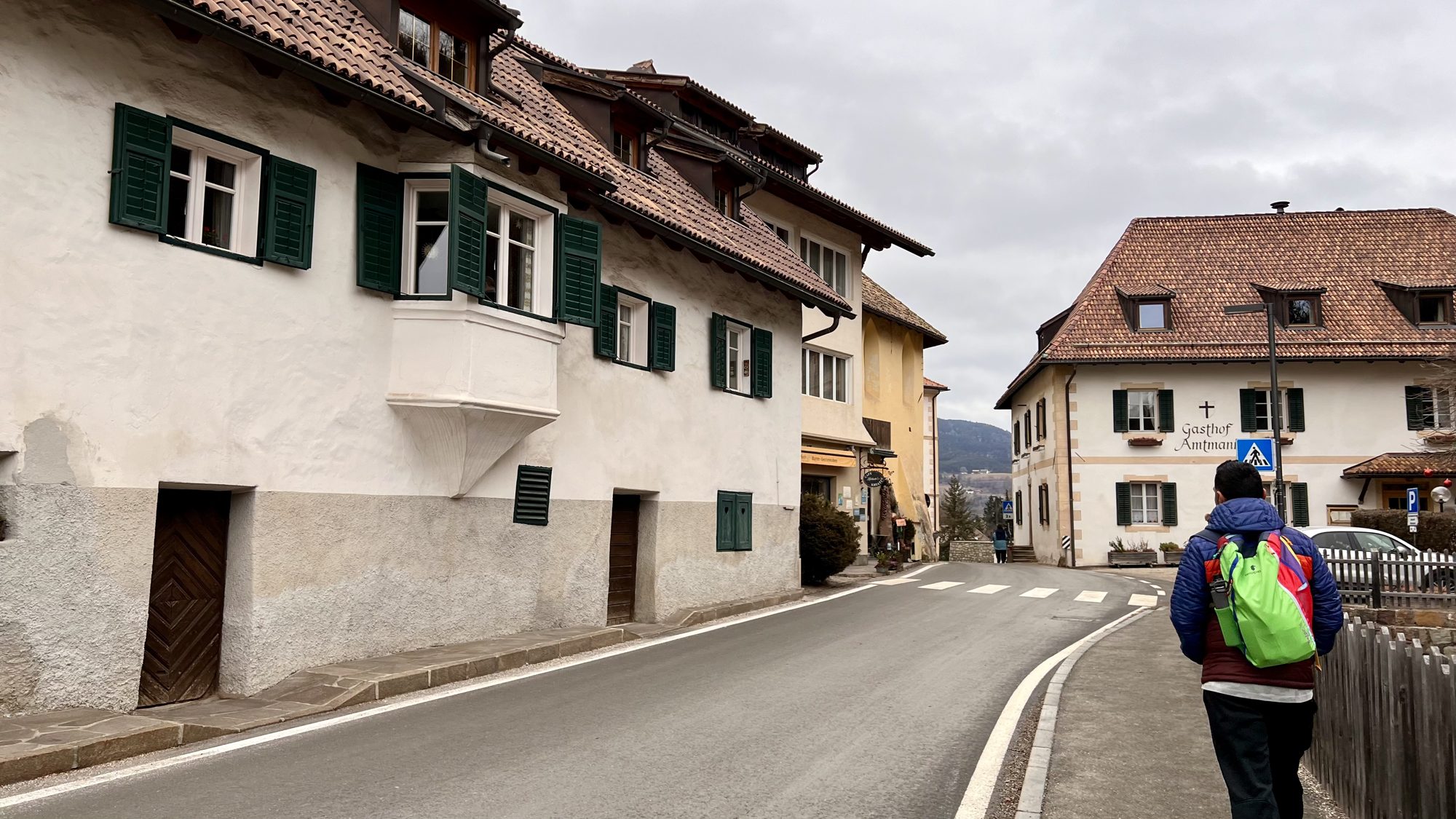 A boy walking along a village street of white houses with green shutters