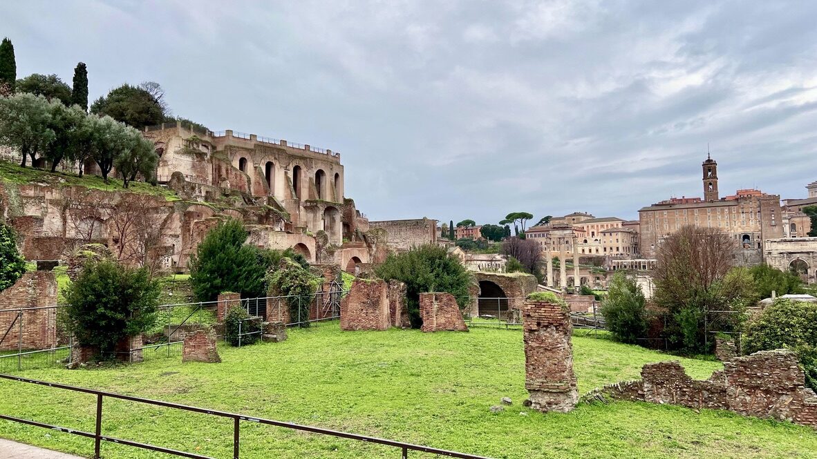 Ruins and green lawns of the Roman Forum under a cloudy sky