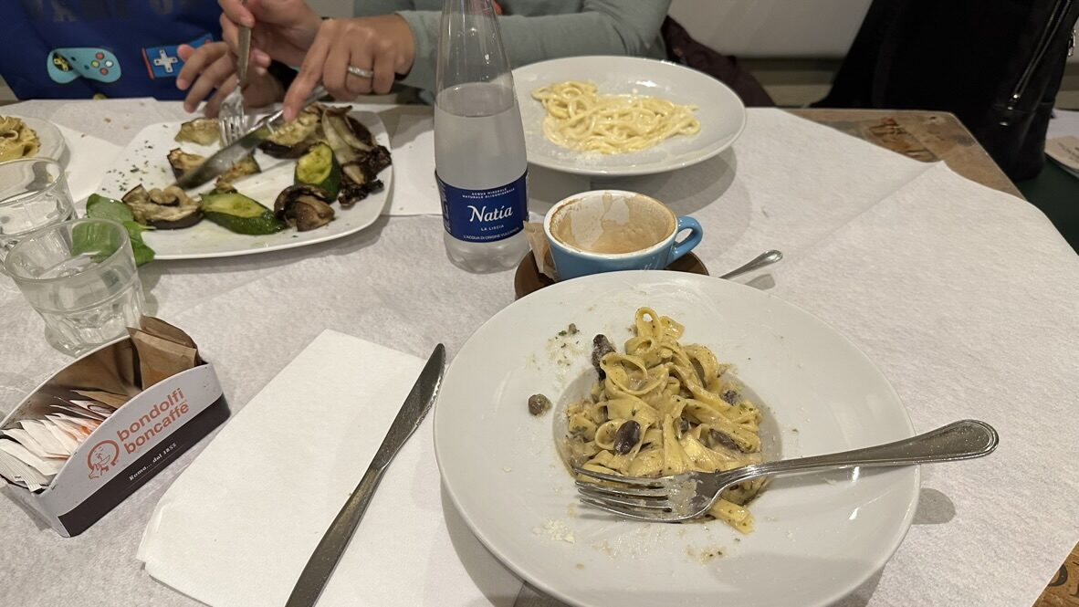 Plates of pasta and grilled vegetables on a restaurant table in Rome