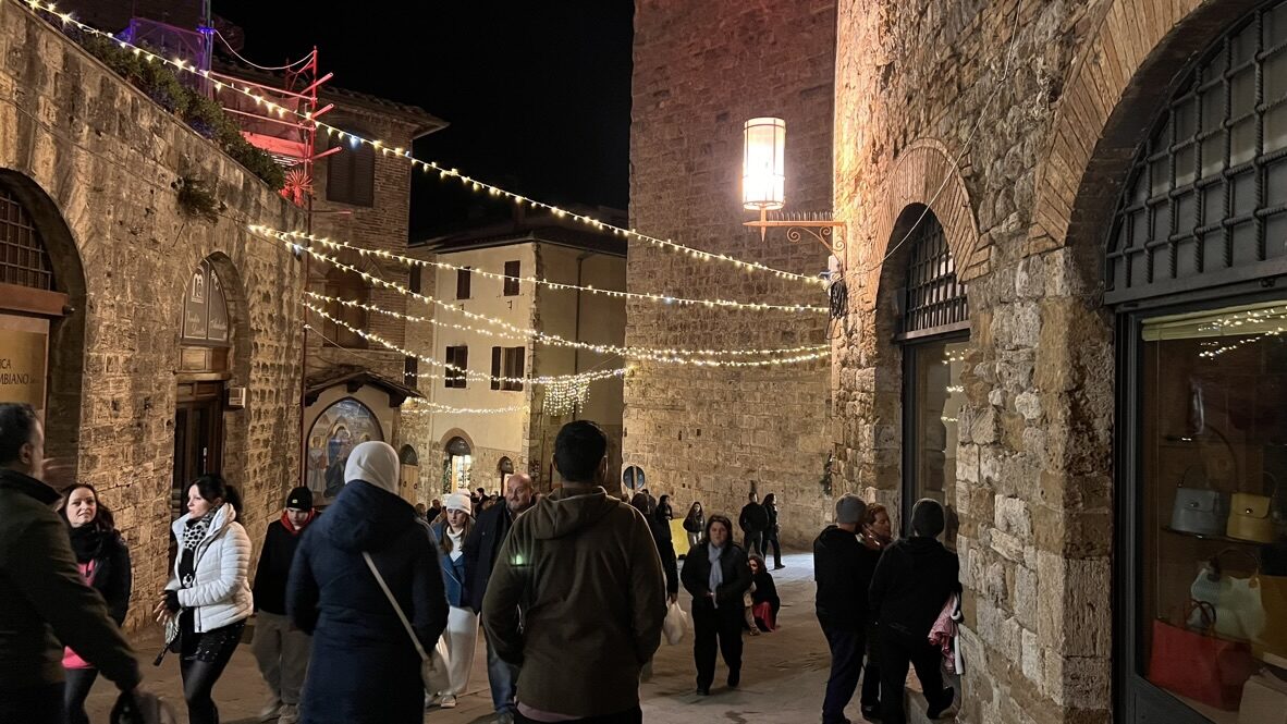 People walking a stone street strung with lights in San Gimignano at night