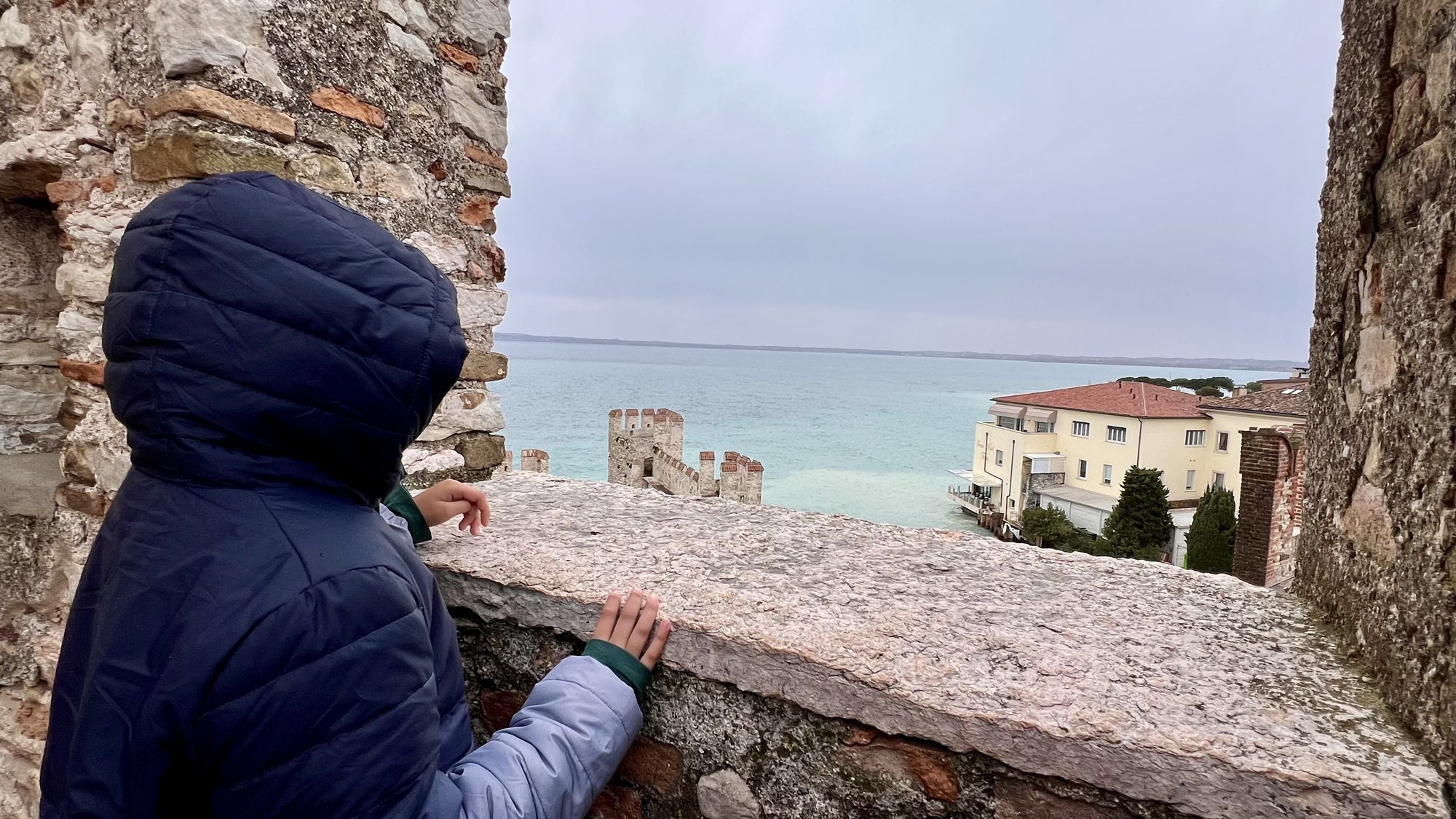 Boy looking over a castle wall at the turquoise lake and rooftops