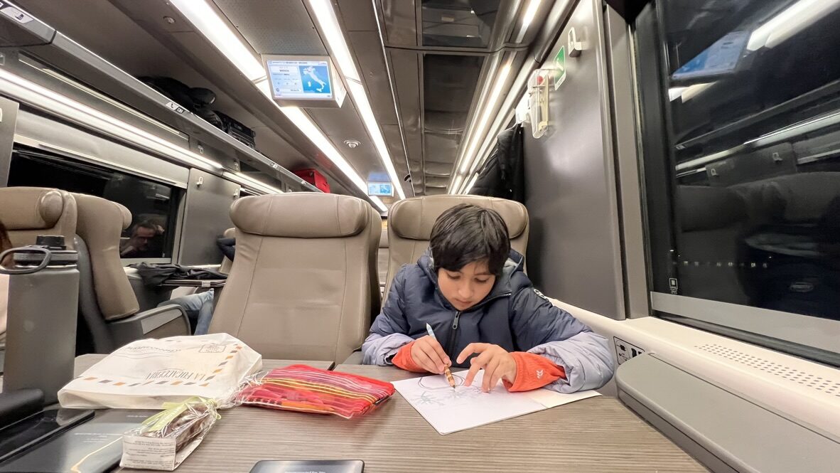 Boy writing at a table in a business class train carriage