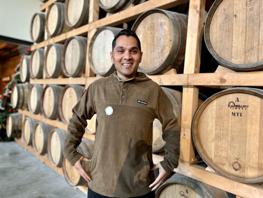 Man smiling in front of racks of wine barrels