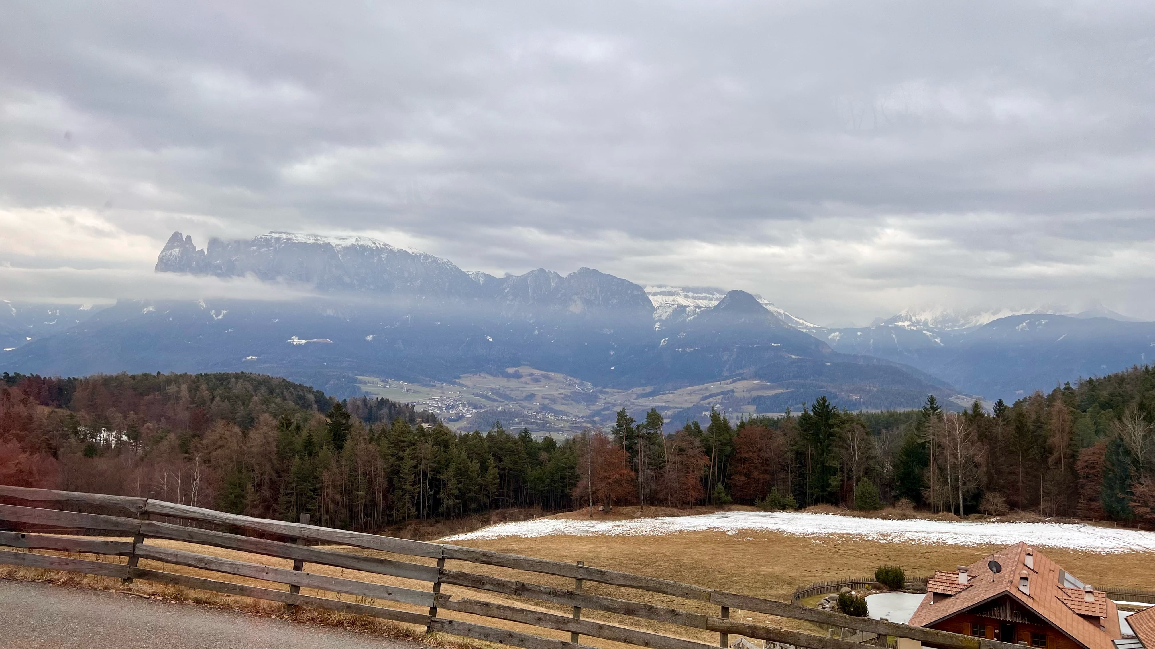 Snow covered mountains in the distance with valley containing a town and roadside fence and houses in a mountain village setting