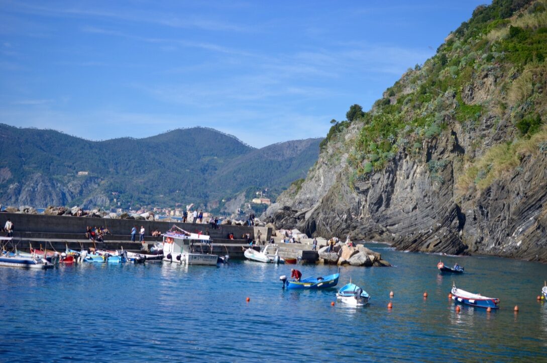 Small boats in the harbor at Vernazza below green cliffs