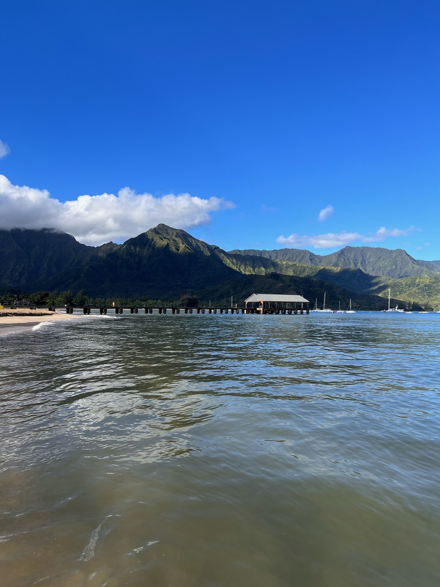 Calm water in Hanalei Bay with the pier and green mountains behind