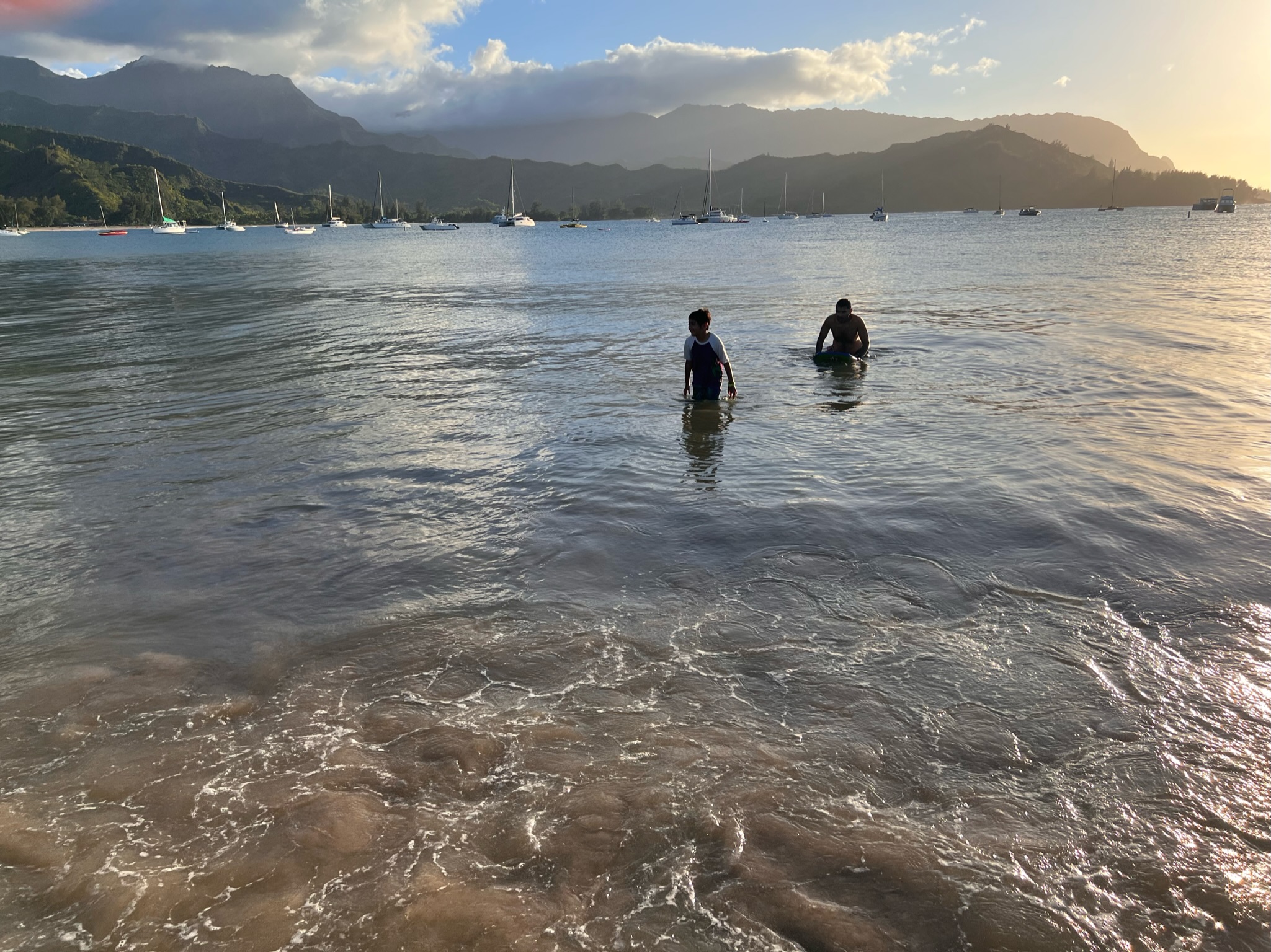 Boy and man coming out of water at the beach in Hanalei bay.