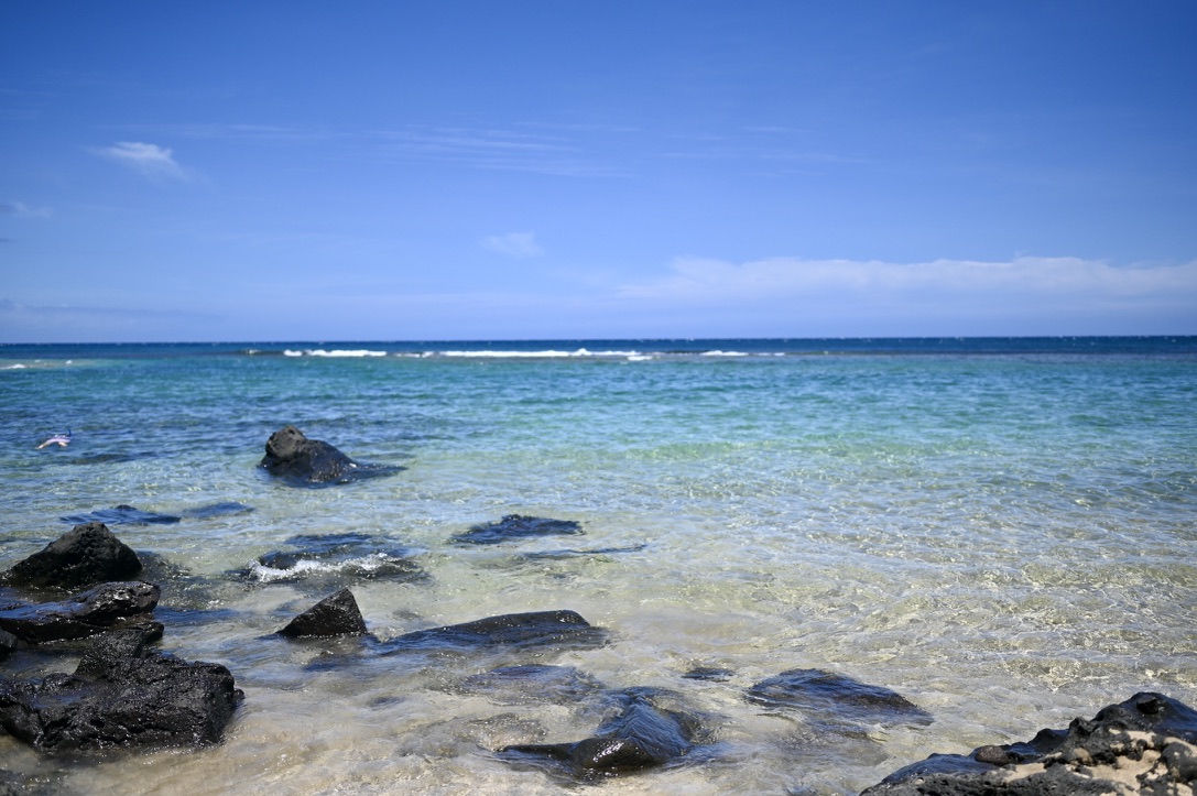 _Blue green ocean by a sandy beach with big rocks.