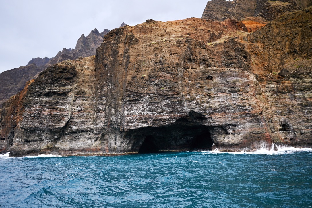 Sea cave on the side of Napali coast's rugged coastline, with blue water and red mountain cliffs