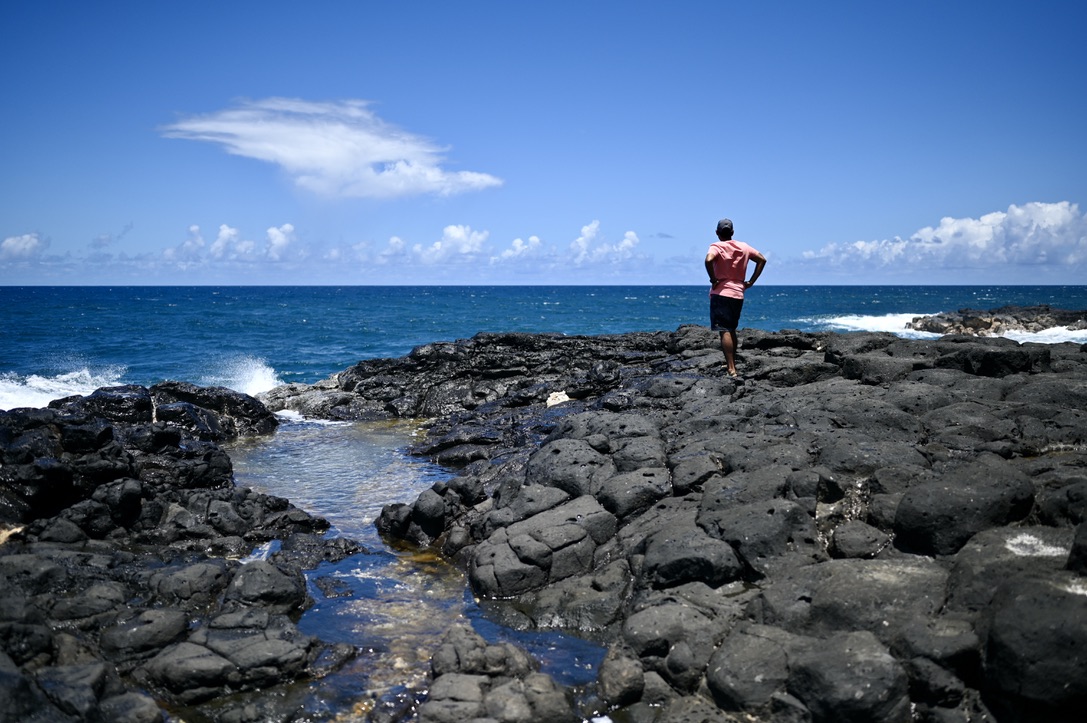 Man looking out at the ocean over rugged volcanic rocks and boulders, with tidal pools around