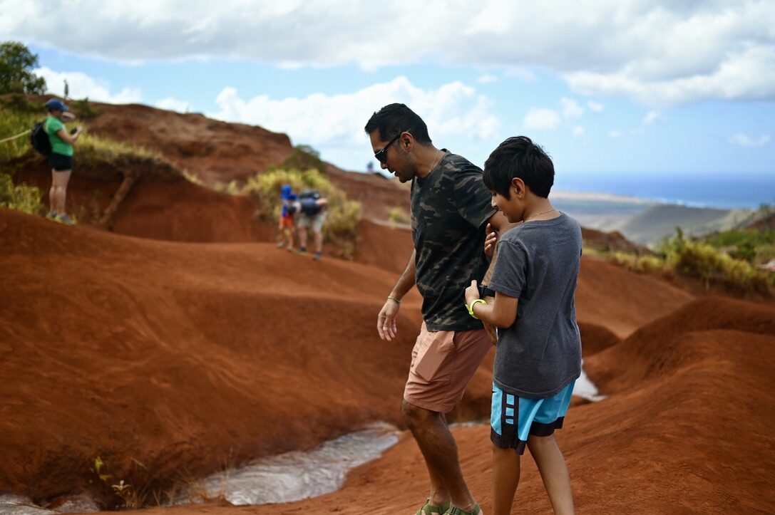 Man and boy walking down red dirt slopes beside a small clear stream