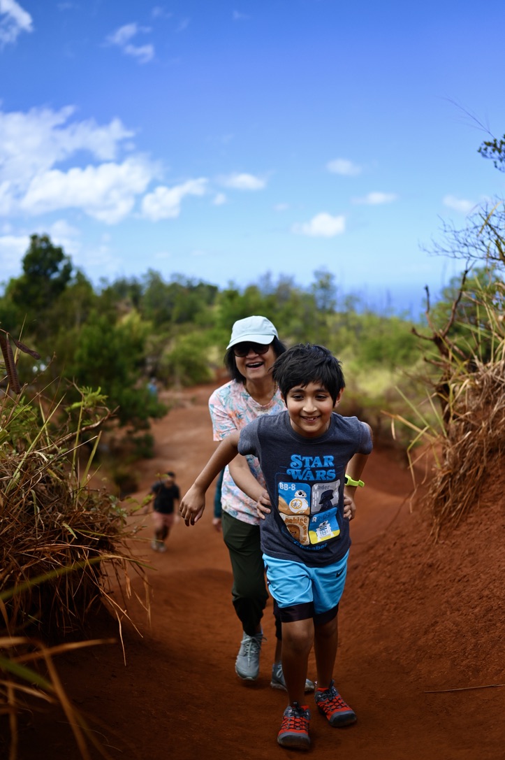 Elder lady and kid laughing and climbing the red dirt mounds in Waimea Canyon State Park area