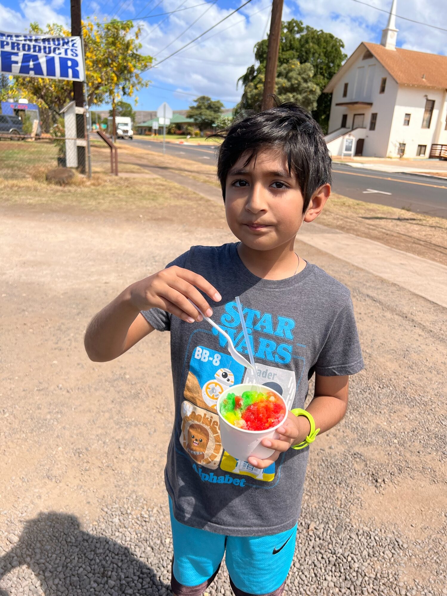 Boy holding a cup of rainbow shave ice by the roadside