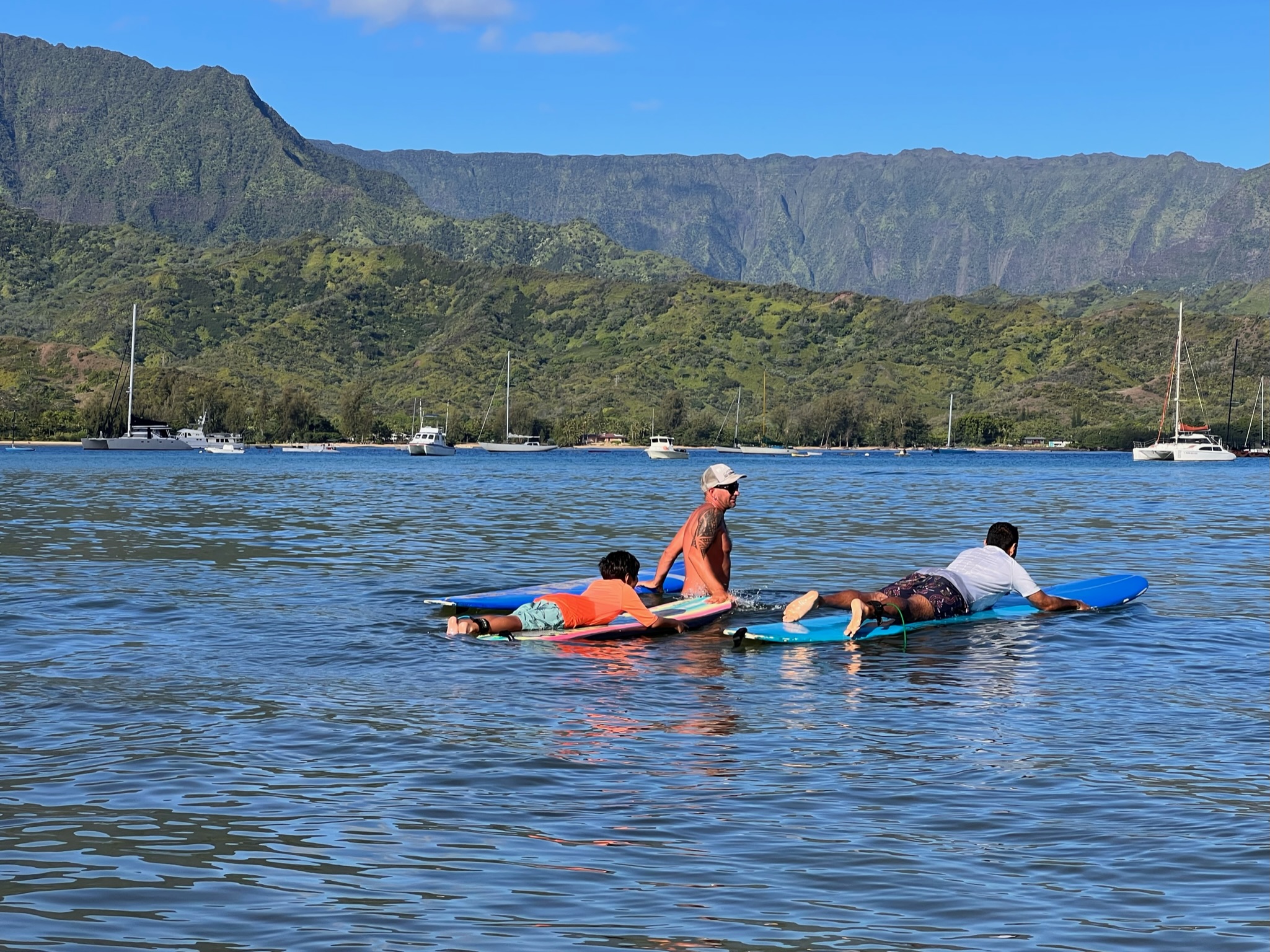 Boy and man learning to surf lying flat on surf board with instructor in the middle at Hanalei bay.