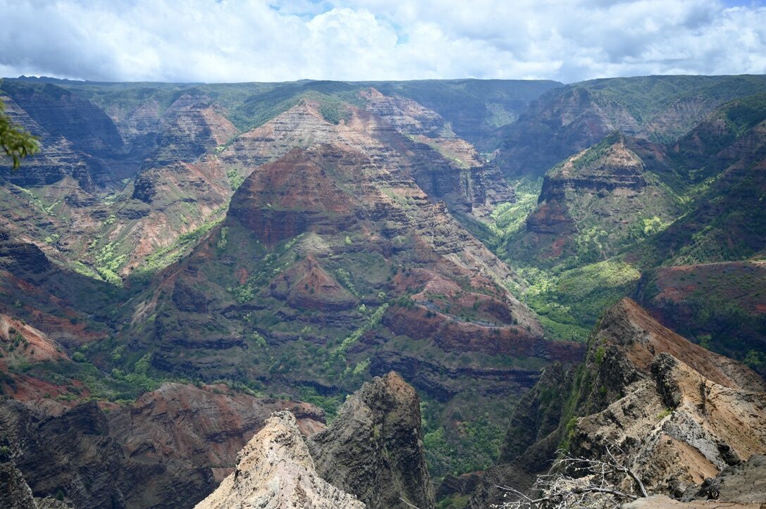 Layered red and green ridges of Waimea Canyon under a cloudy sky