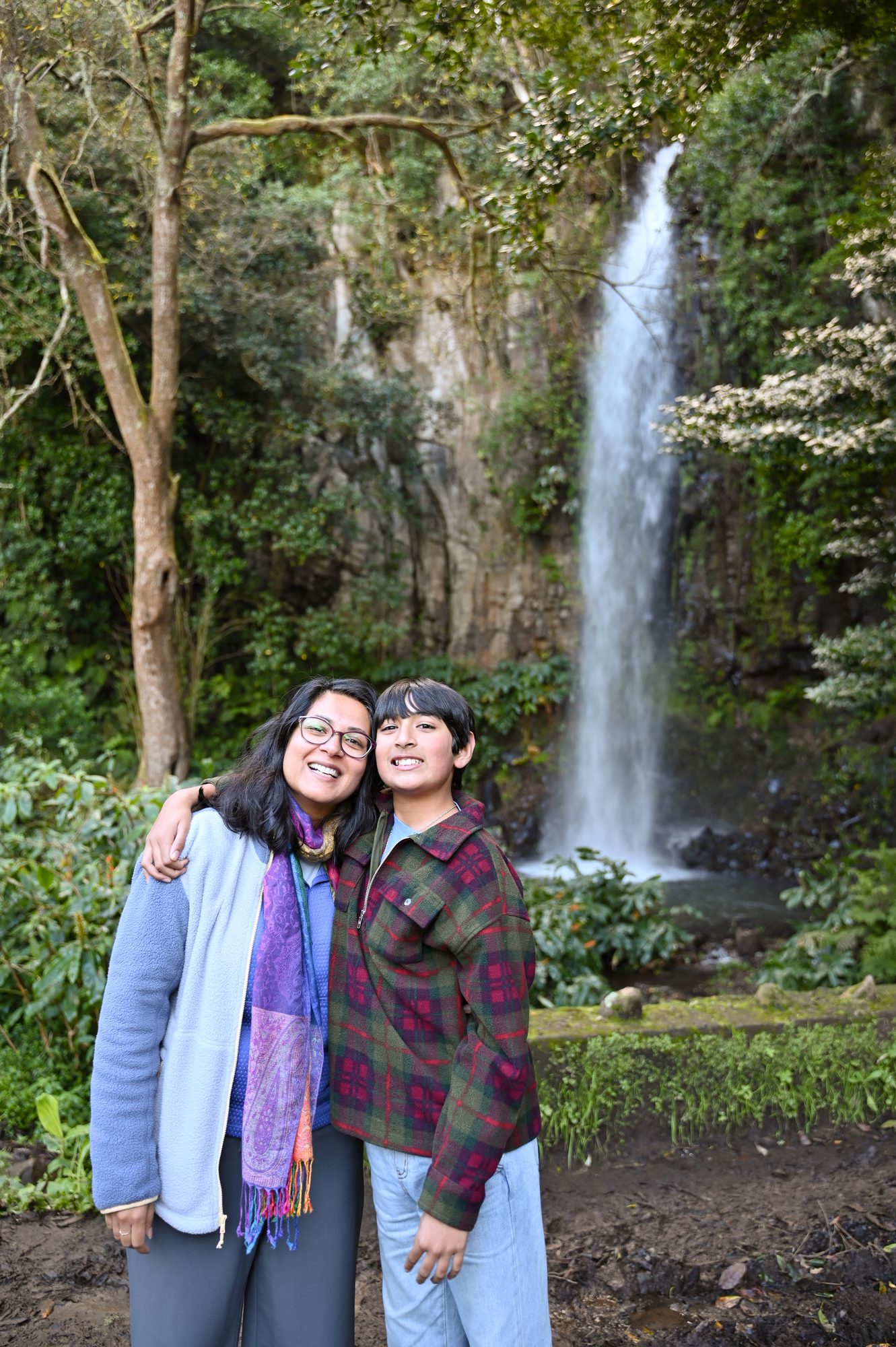 Two of us arm in arm in front of a tall waterfall pouring into a pool in the forest.