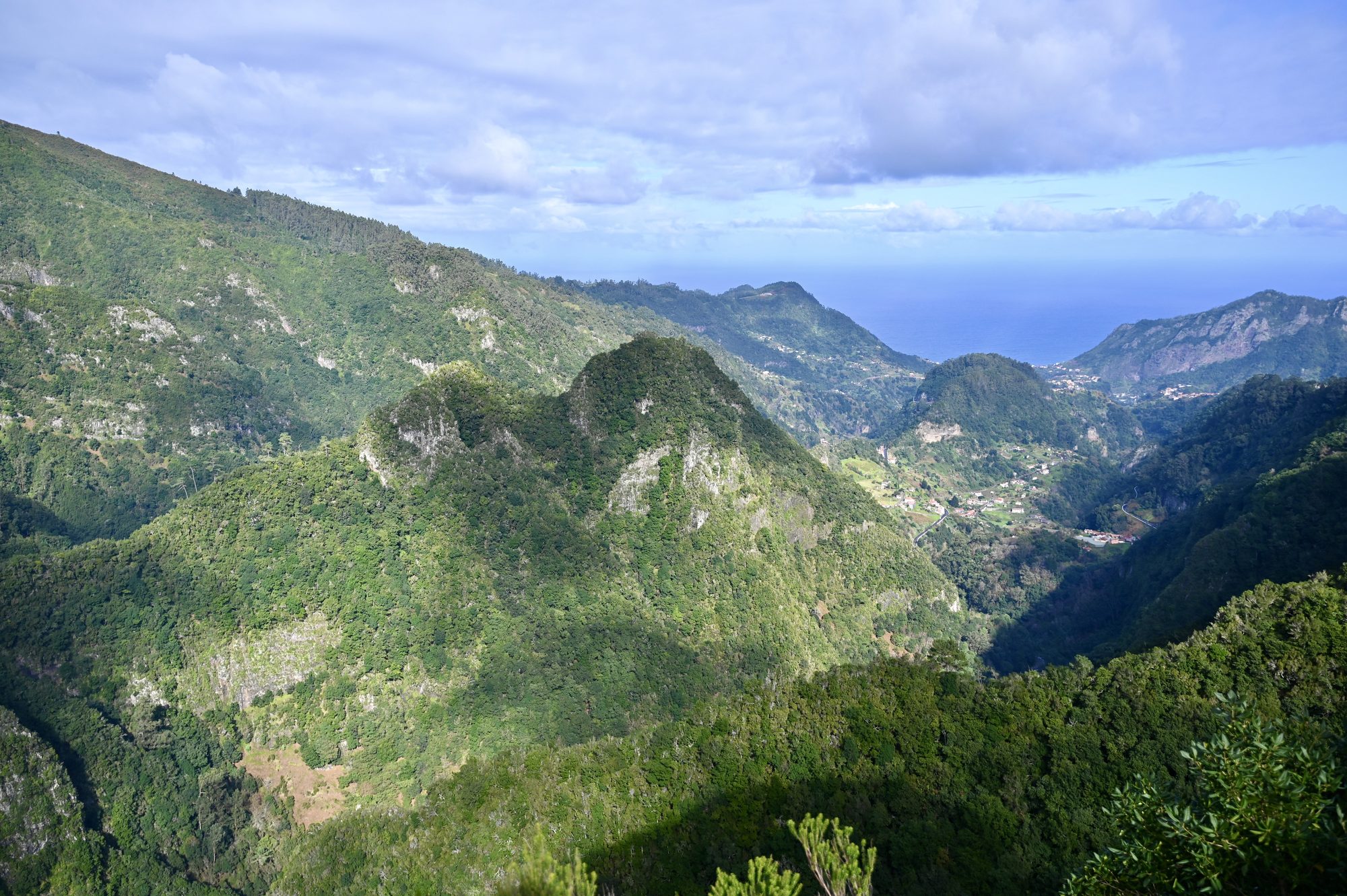 A deep green valley with forested peaks, opening out to the sea in the distance.